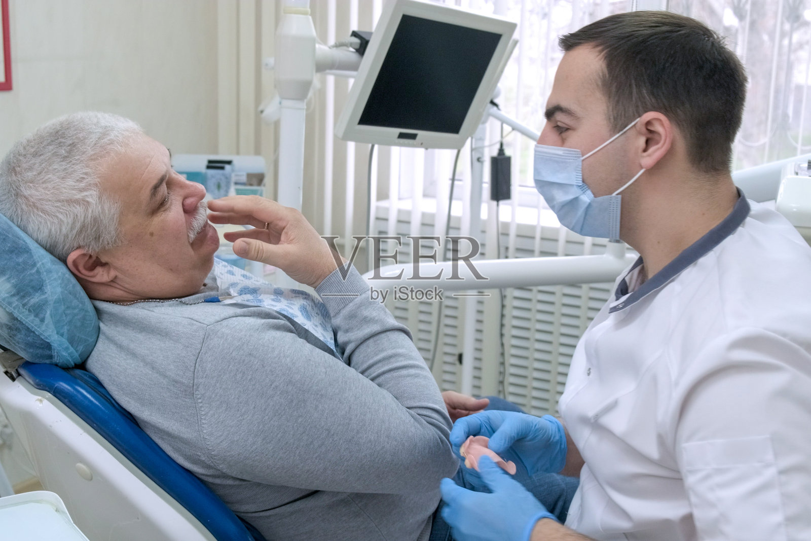 一位老人坐在牙医的椅子上，向医生讲述他的牙齿问题照片摄影图片