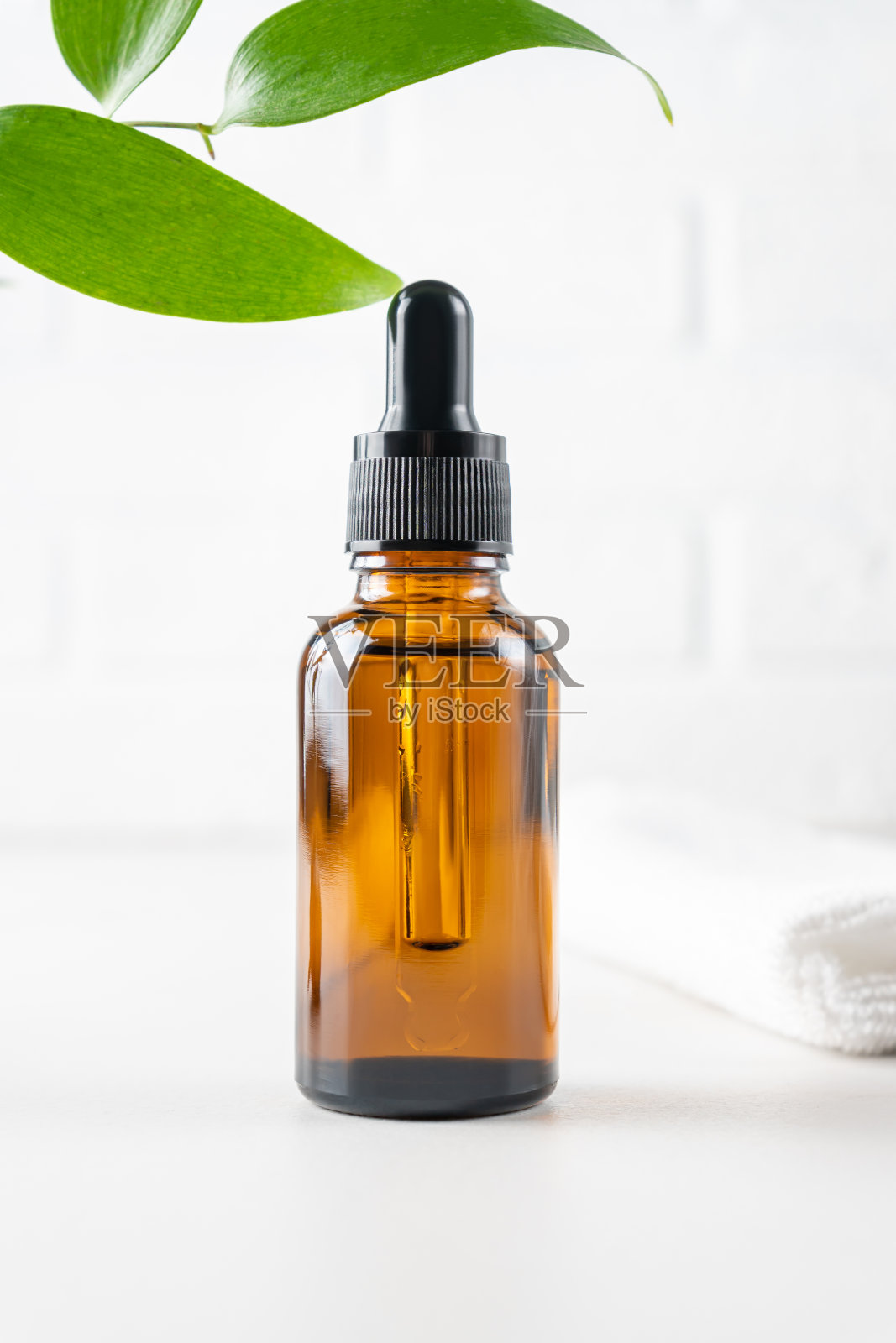 棕色玻璃瓶，装有血清、精油或其他化妆品，白色砖墙背景上有绿叶。天然有机化妆品包装，护肤理念。照片摄影图片