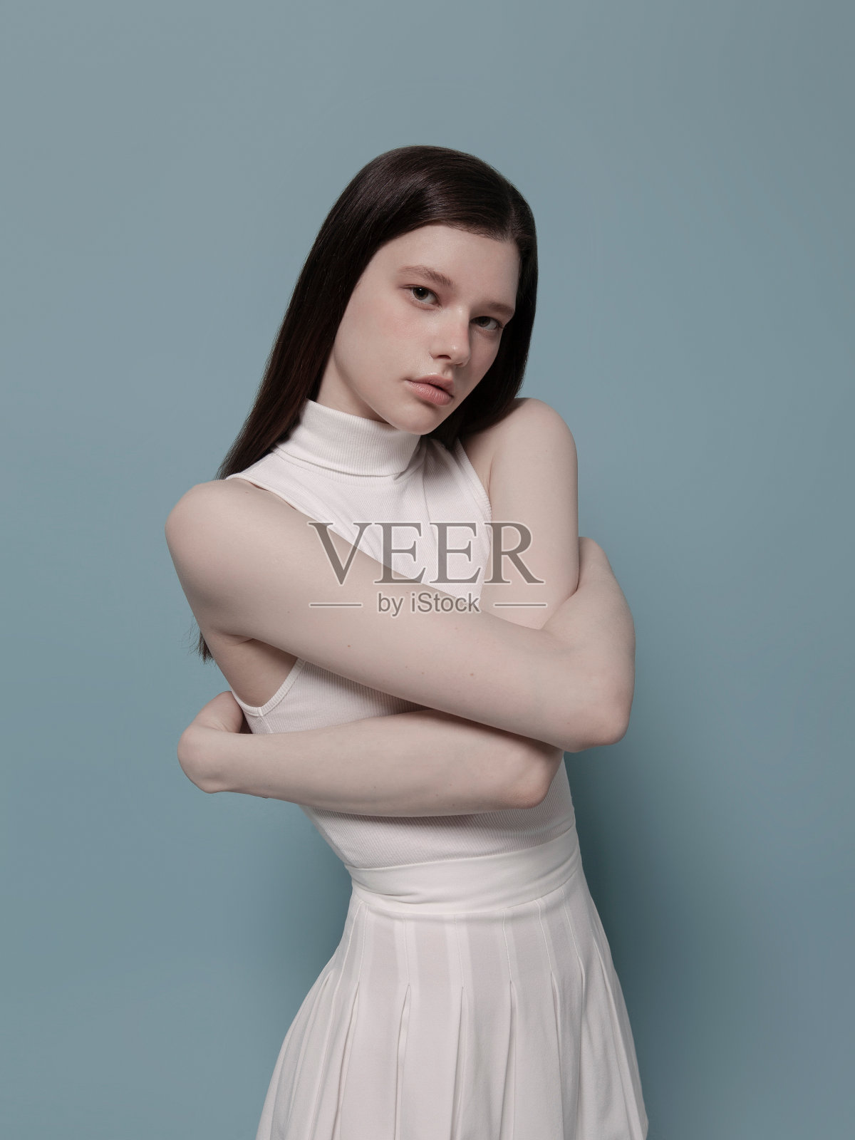 穿着可爱的白色无袖上衣和百褶裙的美丽的年轻女子，韩国风格的K-pop时尚，亚裔白人的混血美人，蓝色背景的时尚模特肖像照片摄影图片