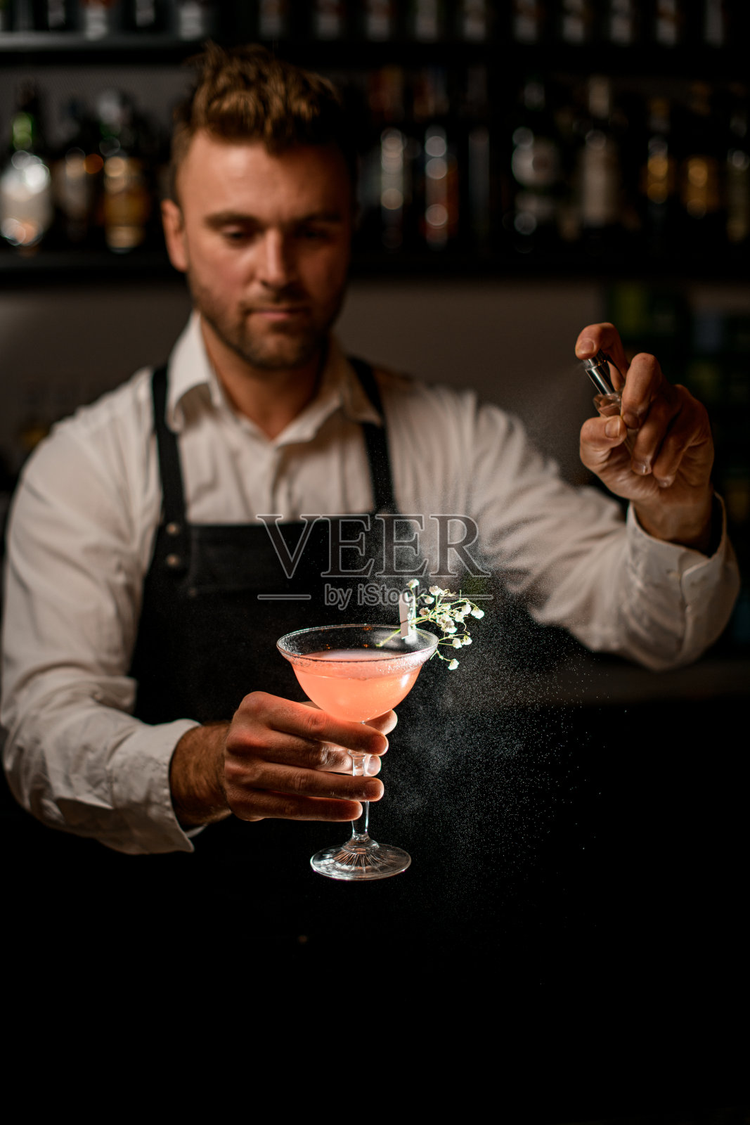 调酒师拿着粉红色的鸡尾酒杯，从小瓶里往上面喷酒照片摄影图片