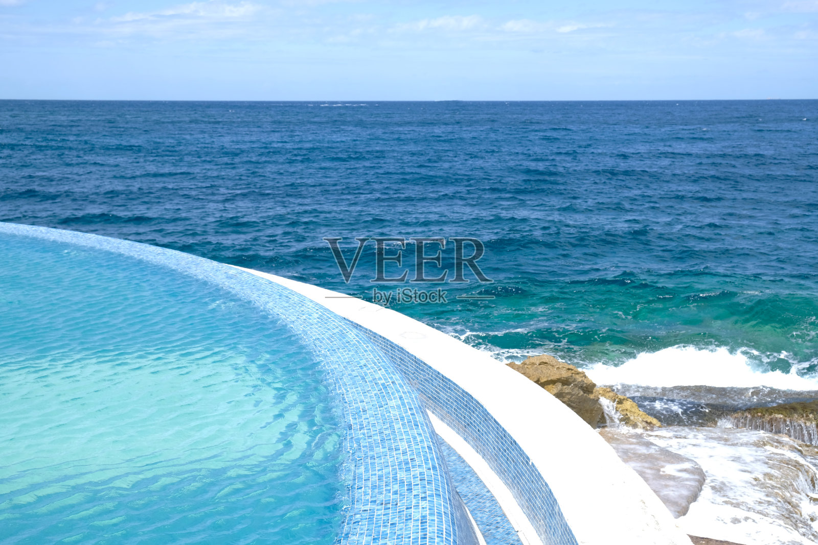 蓝色清澈的水面游泳池在一个度假胜地的海景。暑假和休息的概念。豪华海滩别墅。蓝色瓷砖马赛克图案。照片摄影图片