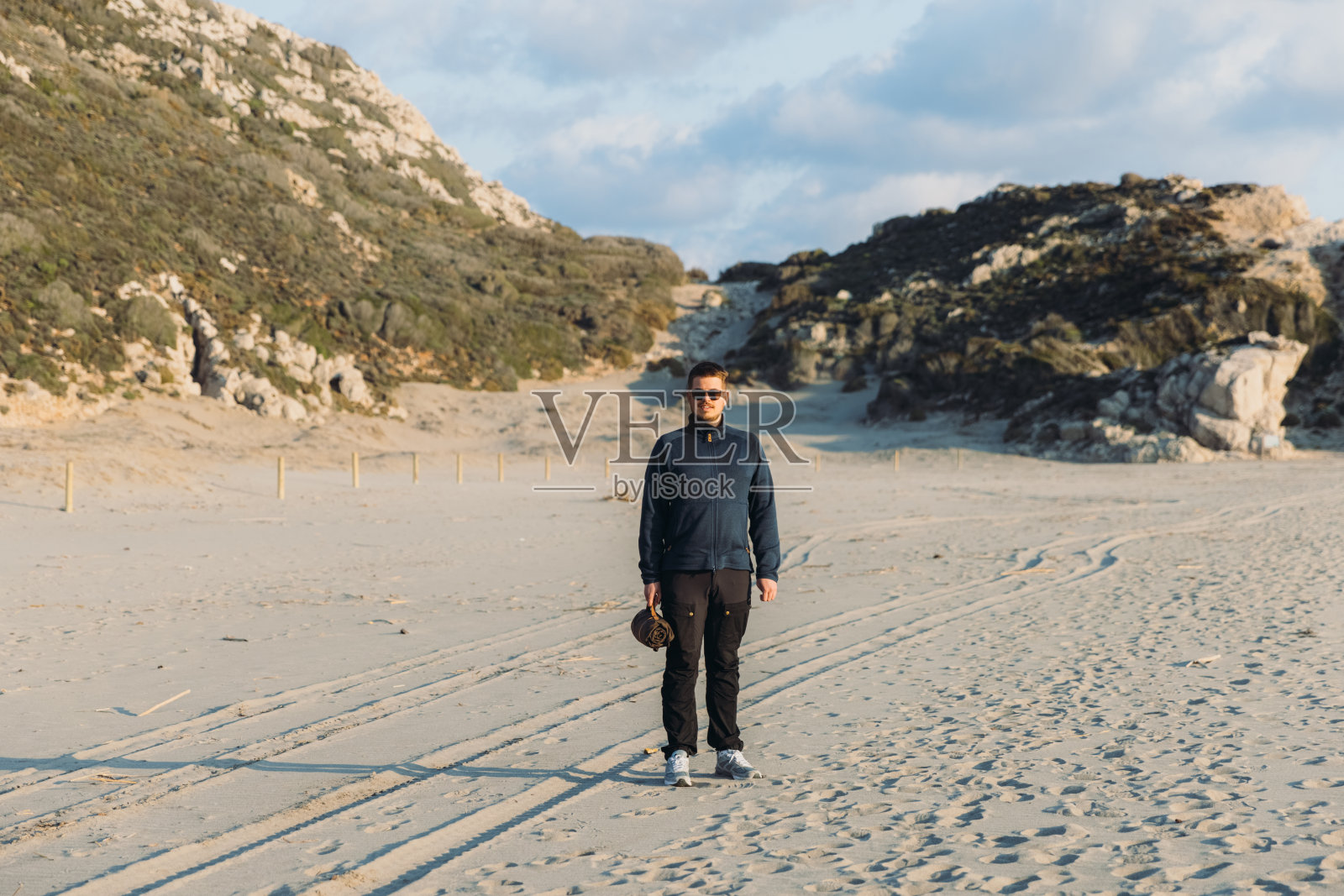 在土耳其日落期间，男子在海边散步，带着野餐毯子照片摄影图片