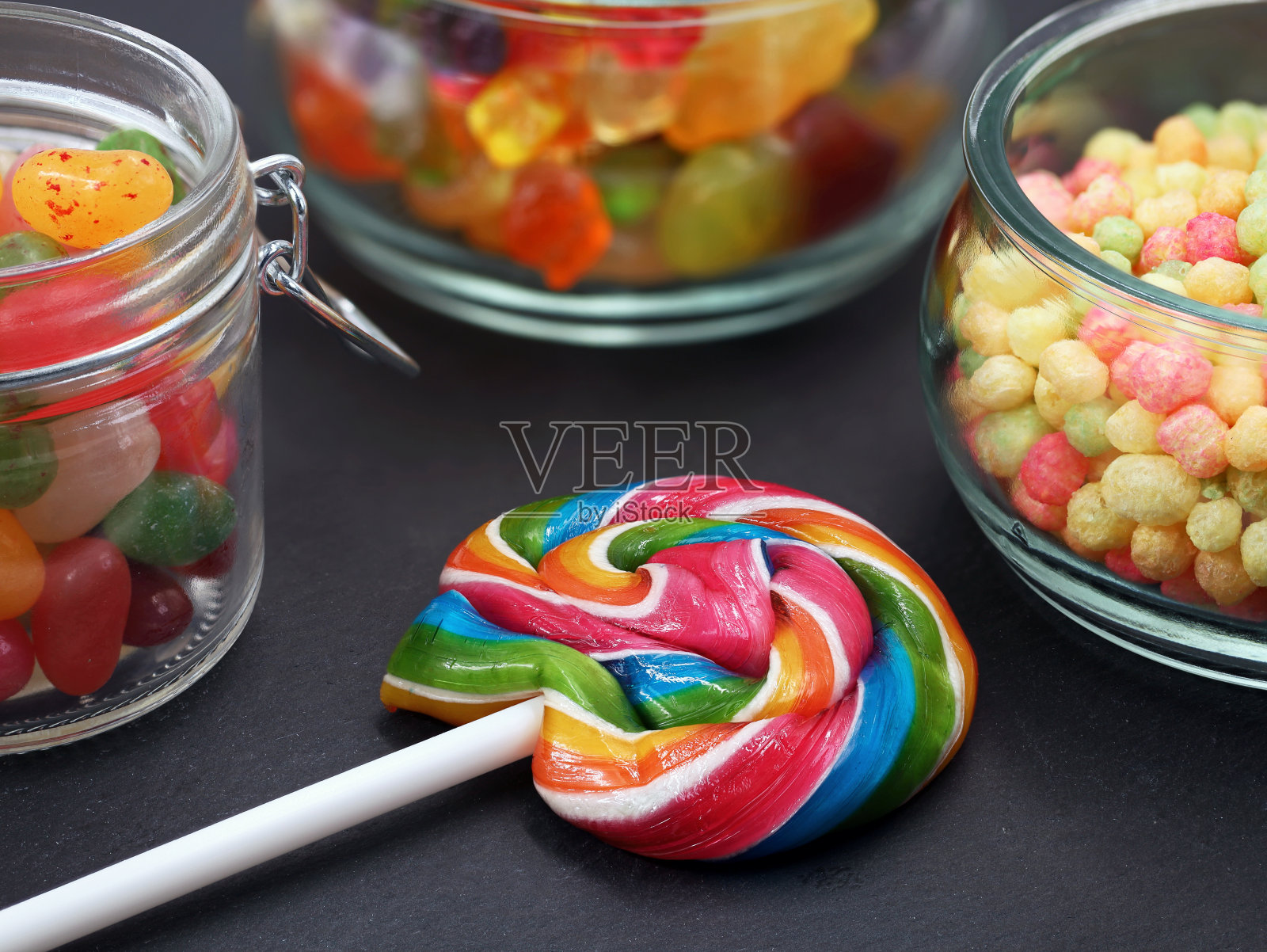 彩色的棒棒糖和各种糖果在罐子上的黑色背景，接近照片摄影图片