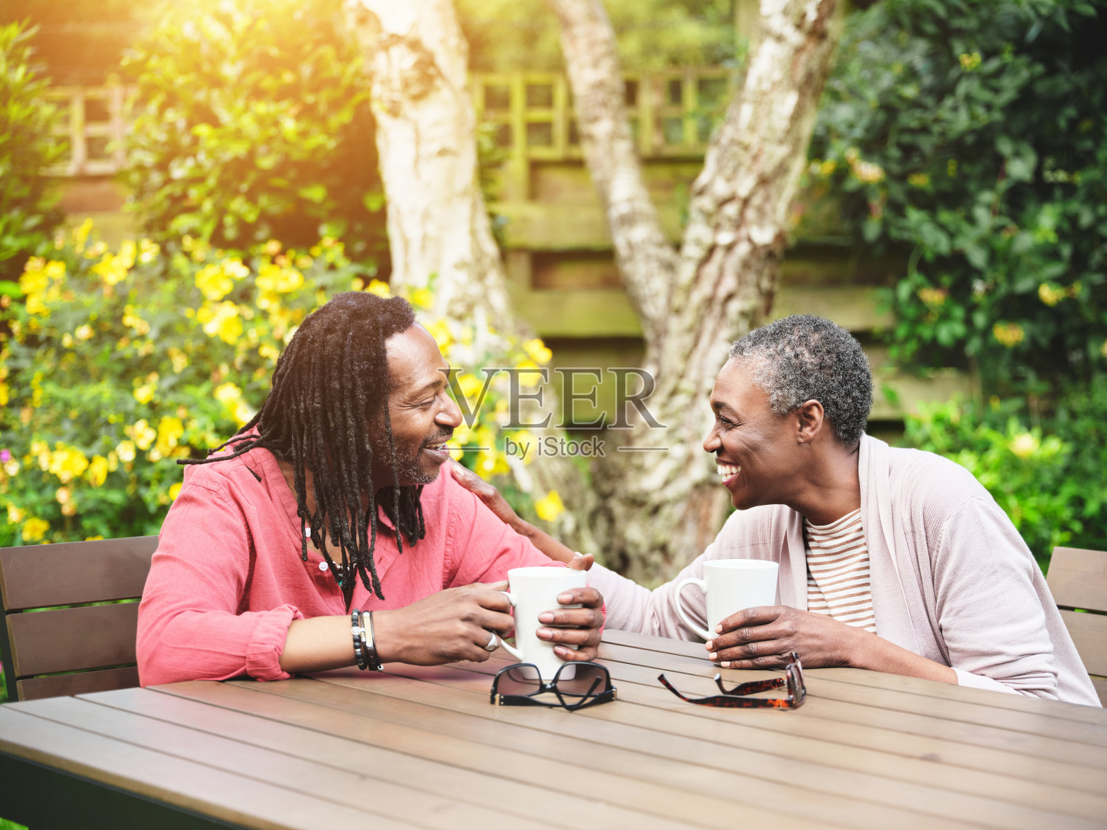 一对幸福成熟的情侣坐在室外的花园里，一起喝着咖啡。面带微笑的老男人和老女人一边喝茶休息，一边聊天照片摄影图片