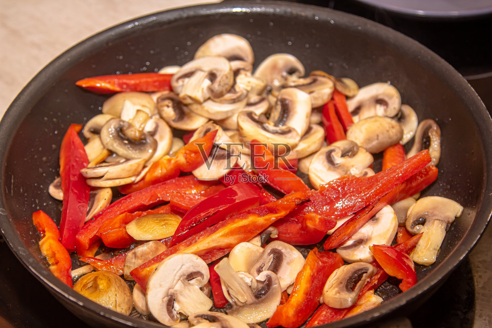 蘑菇、红洋葱、红黄甜椒在平底锅里用旧木铲煎炸照片摄影图片
