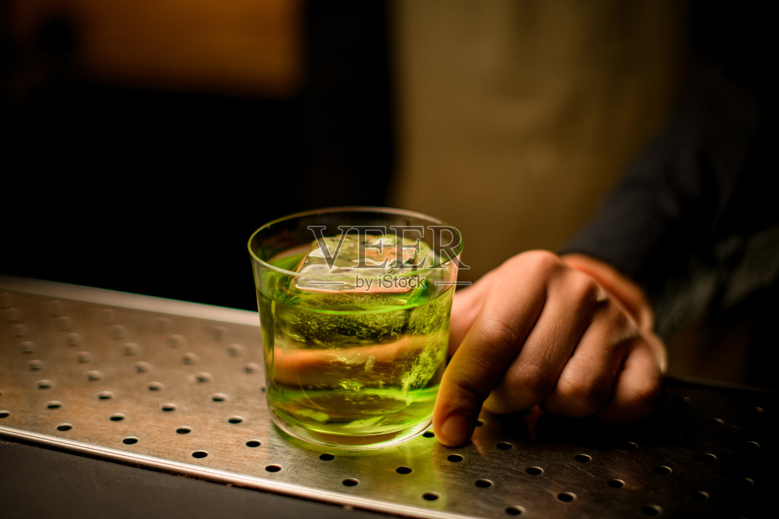 特写镜头的玻璃饮料与冰块站在吧台和手的男招待员拿着它照片摄影图片