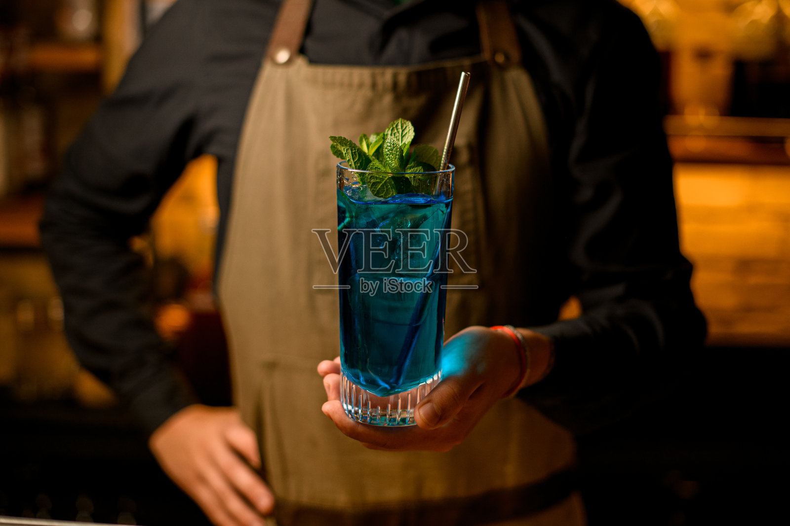 美丽的景色玻璃蓝色冷饮与钢喝吸管和绿色薄荷叶在男招待员的手照片摄影图片
