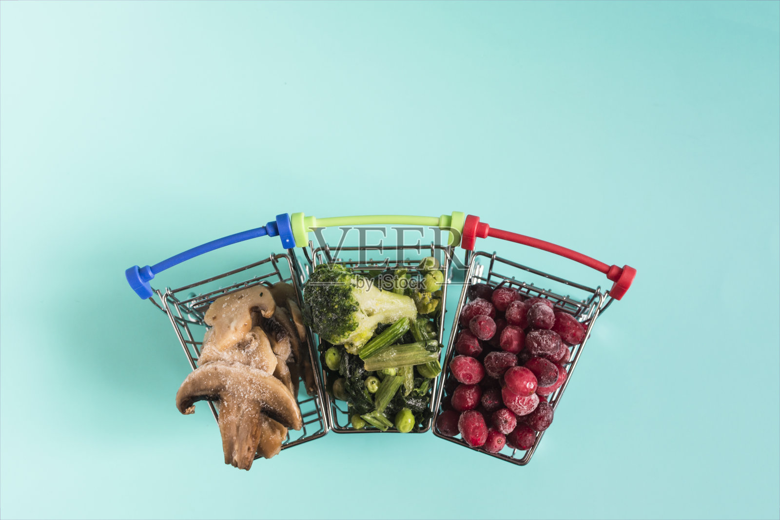 在蓝色的kopi空间背景下，冷冻的绿色蔬菜、浆果和蘑菇和冰晶堆积在杂货店的篮子里。照片摄影图片