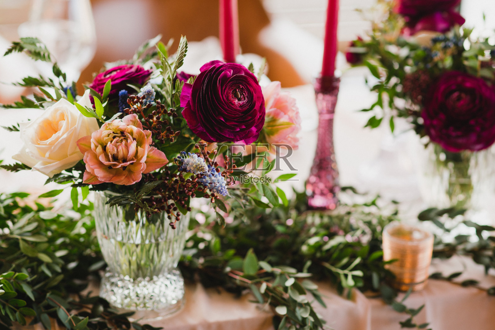 花卉组成与美丽的毛茛花和绿色植物，蜡烛，铺设和盘子在一个装饰的桌子。照片摄影图片