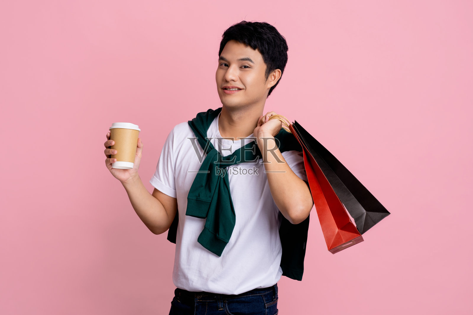 年轻的亚洲人与彩色纸袋孤立在浅粉色的背景。照片摄影图片