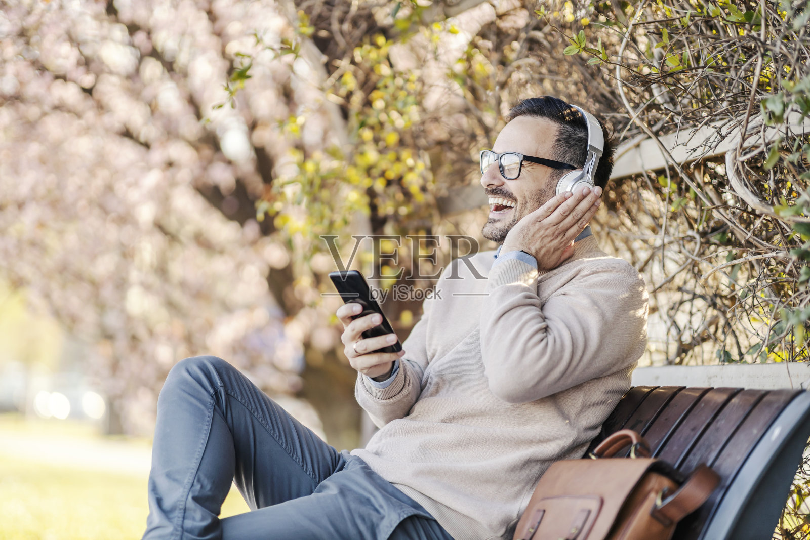 一个快乐的男人坐在公园里听着电话里的音乐。照片摄影图片