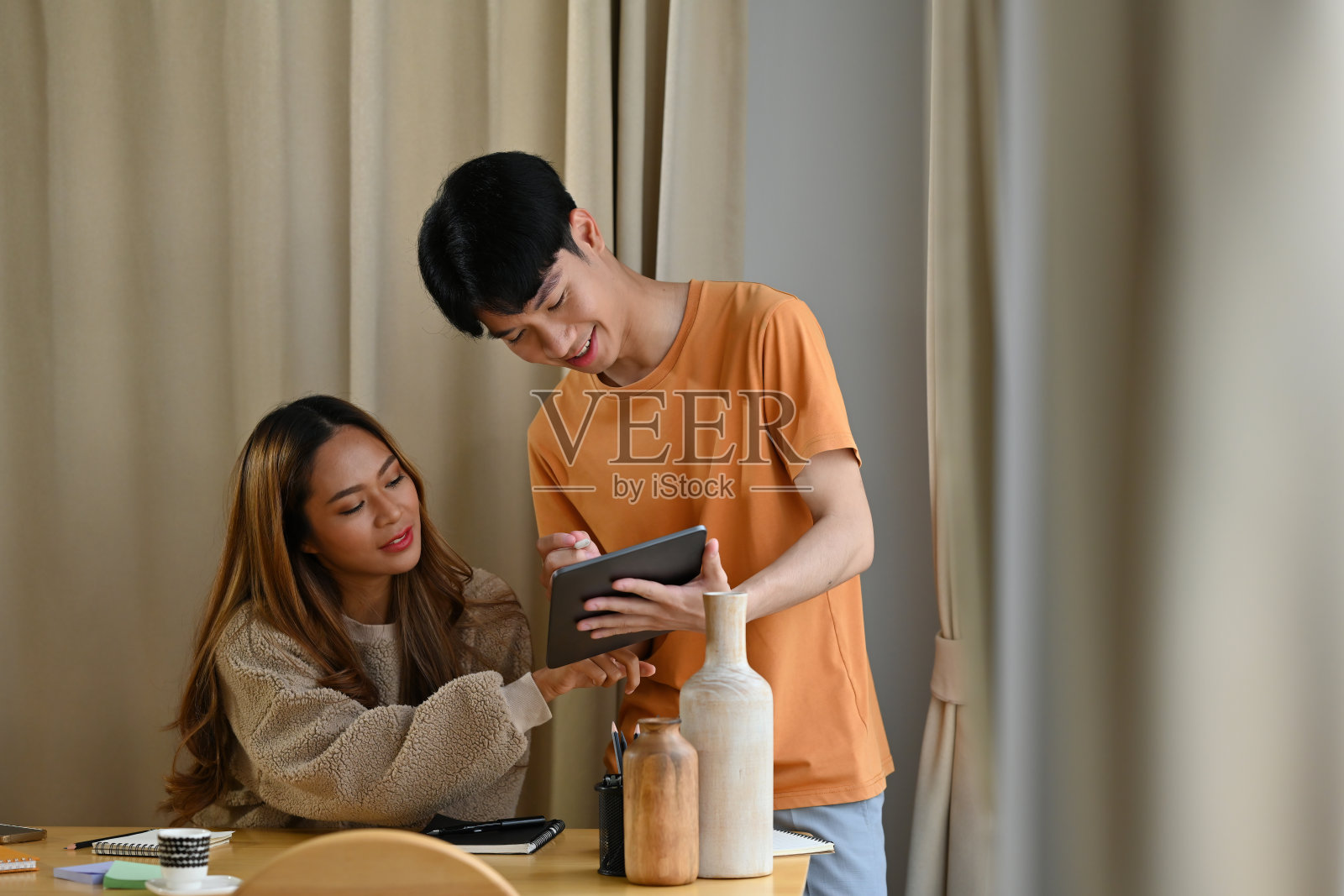 快乐的亚洲男人和女人坐在客厅里，一起在平板电脑上计划一个项目。为家庭和工作的概念照片摄影图片