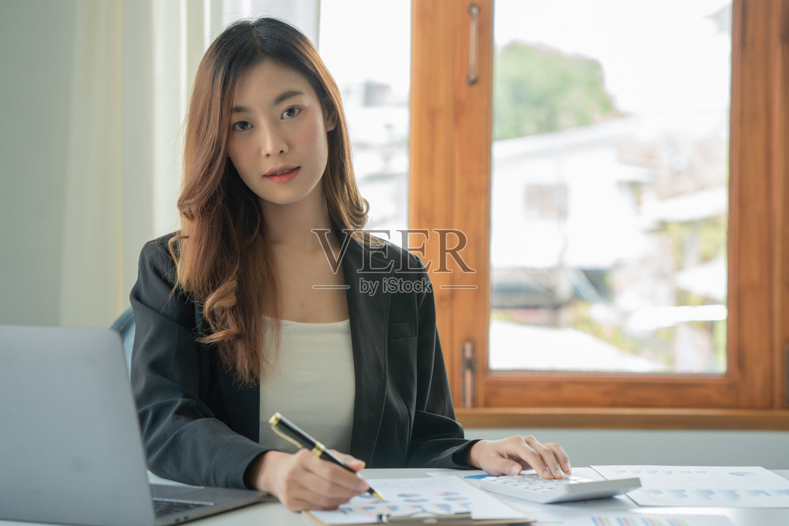 年轻女性使用计算器，另一只手使用钢笔，在书中做笔记，在咖啡馆或同事的工作空间的桌子上有笔记本。共同工作空间的概念。照片摄影图片