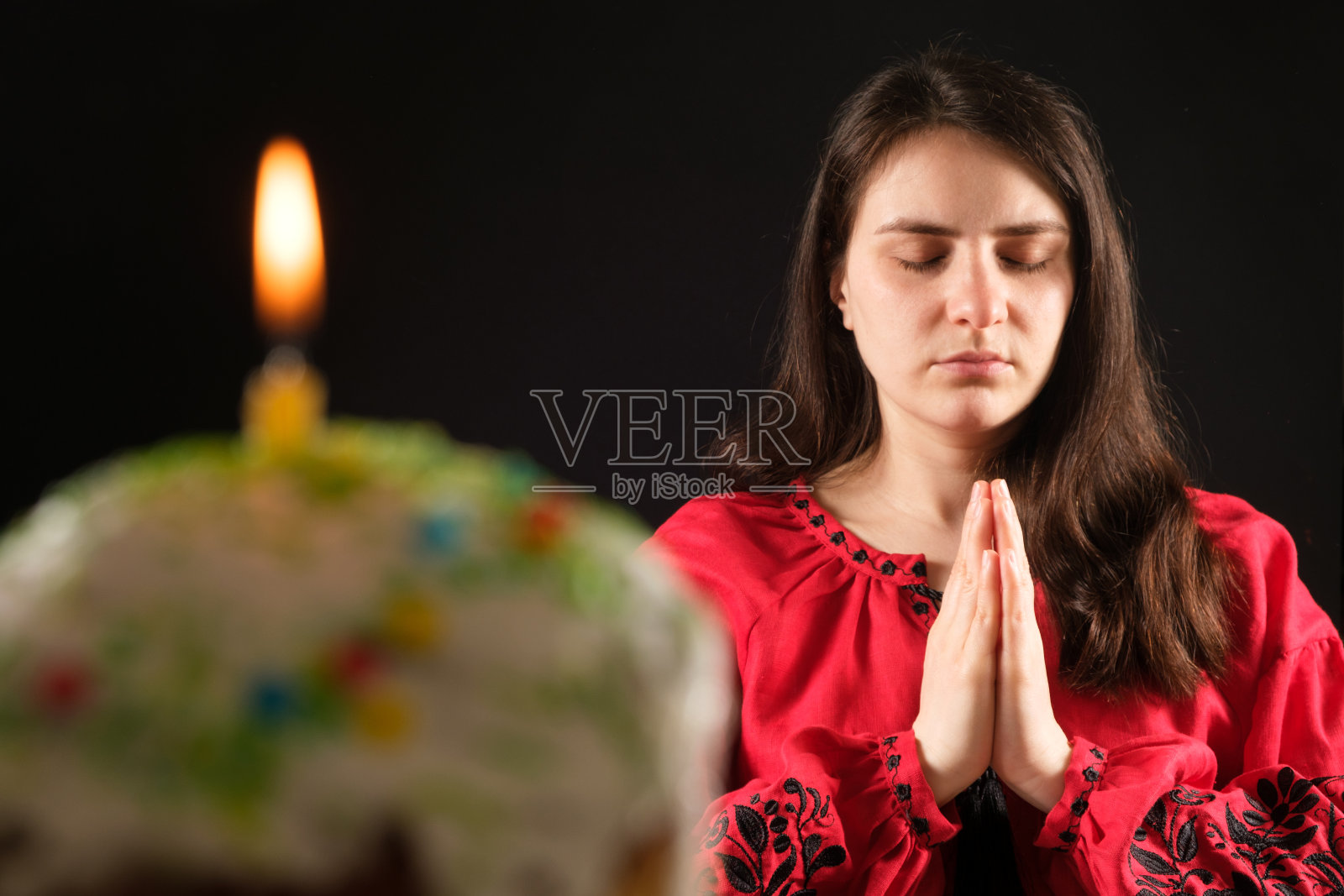 一个祈祷的女人和一个带着蜡烛的复活节蛋糕。照片摄影图片
