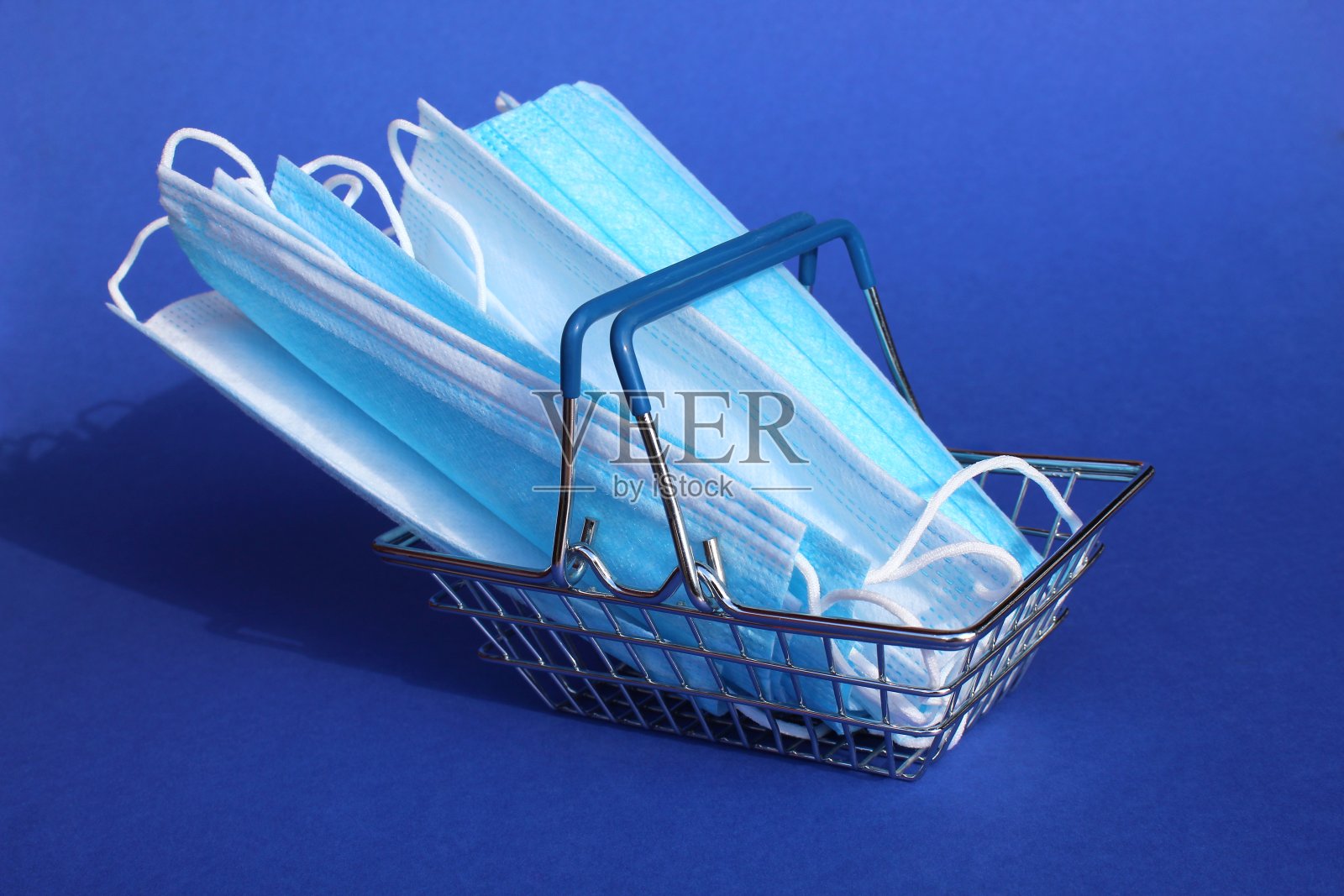 医用口罩放在蓝色背景下的小型购物篮里。照片摄影图片