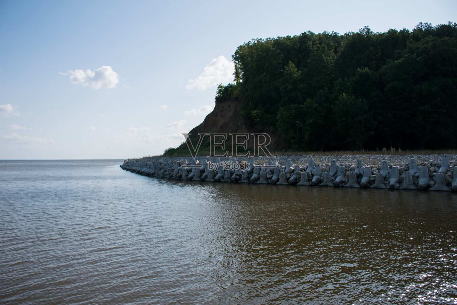 夏季景观，陡峭的河岸上有树木，下面狭窄的卵石海滩上有障碍物照片摄影图片