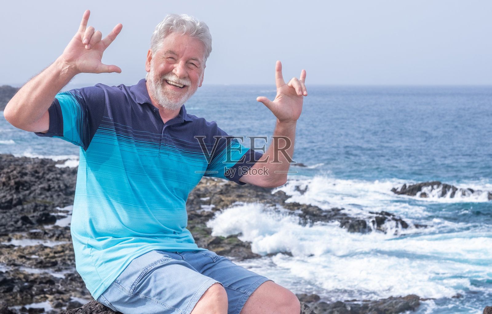 迷人的肖像快乐的年老男子穿着蓝色t恤享受户外度假在海上。满脸胡须的上了年纪的男性看着镜头用手做手势。假期或退休的概念照片摄影图片