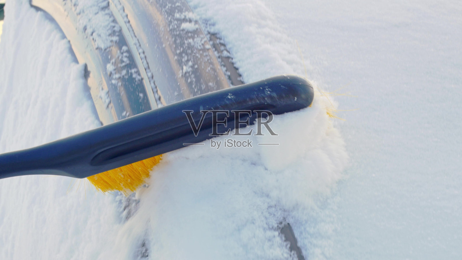 冬天，车被雪覆盖，出行前需要用刷子把车上的雪擦干净。清扫汽车上的积雪，清扫暴风雪后挡风玻璃上的积雪照片摄影图片