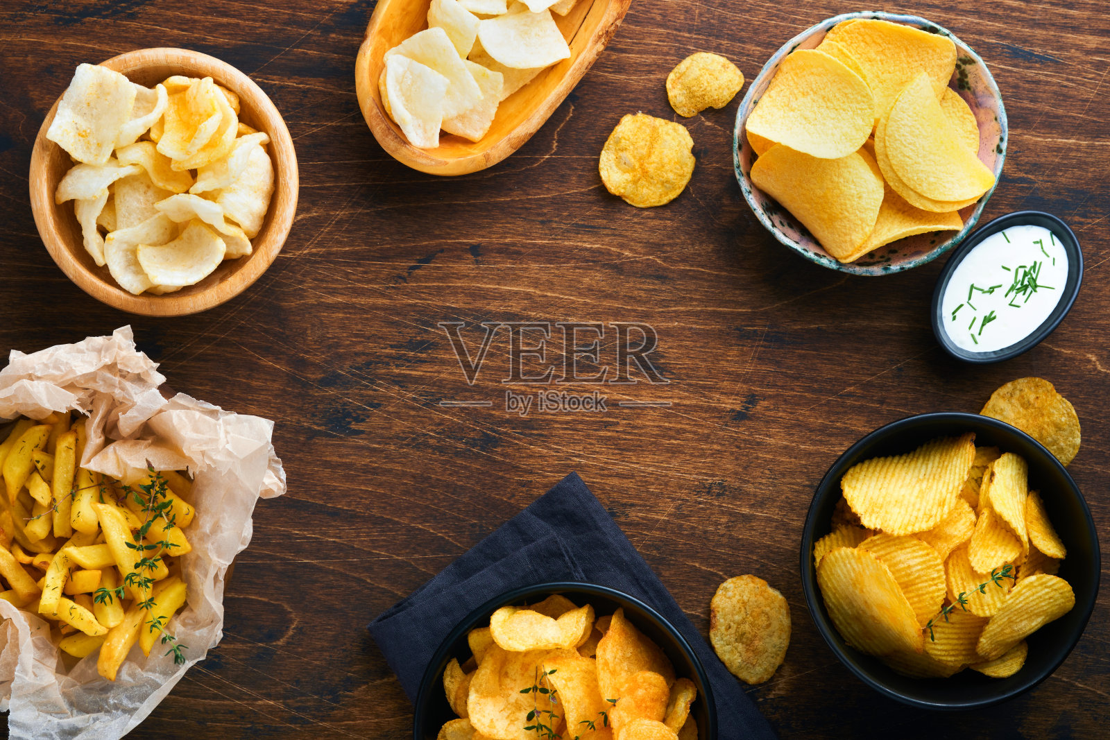 不健康的食物或零食。所有经典的土豆小吃，花生，爆米花，洋葱圈和咸味椒盐脆饼放在碗盘里，在旧的木制背景上。对身材、心脏、皮肤、牙齿都不健康。照片摄影图片