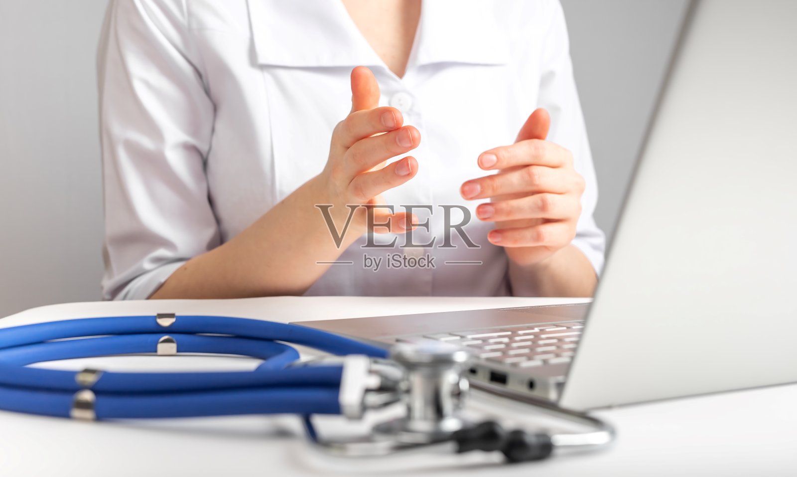 医生给病人进行在线咨询。医疗保健和远程医疗概念。远程病人检查和治疗疾病。穿着实验服的女人坐在桌前，拿着笔记本电脑和听诊器照片摄影图片