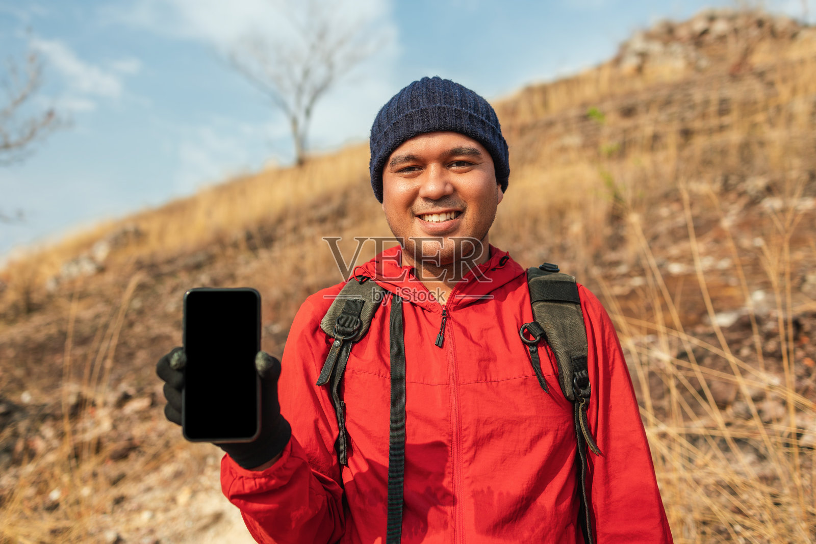 男人旅行者拿着智能手机在假期冒险旅行。背包客站在山顶展示手机。照片摄影图片
