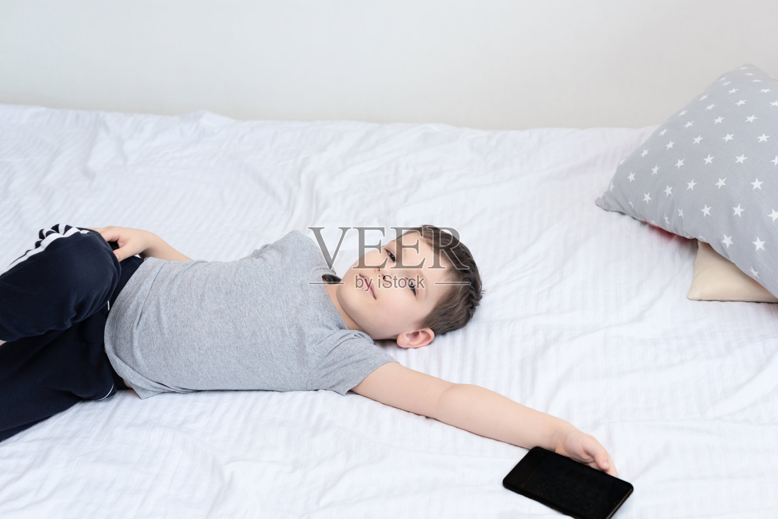 男孩躺在床上，用智能手机玩游戏或学习。社会与科技概念照片摄影图片