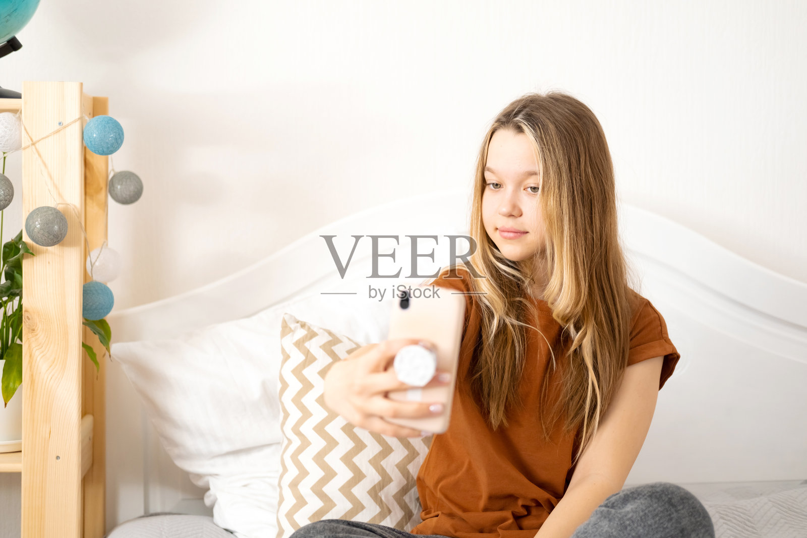 美丽的白人少女在家里用她的智能手机自拍，微笑，有乐趣，欣赏自己。照片摄影图片