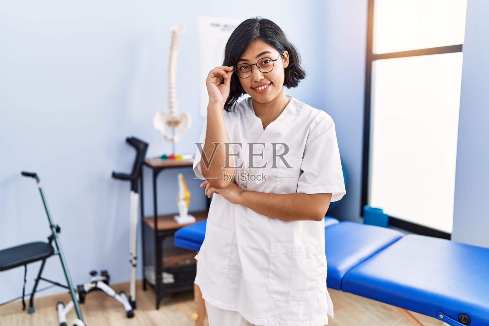 身穿理疗师制服的年轻拉丁女子在理疗诊所站着，双臂交叉照片摄影图片