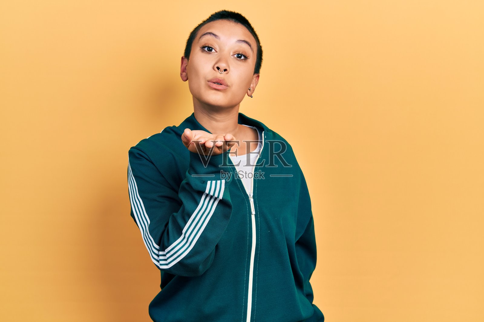 美丽的西班牙女人与短头发穿运动夹克看相机飞吻与手在空气可爱和性感。爱的表达。照片摄影图片