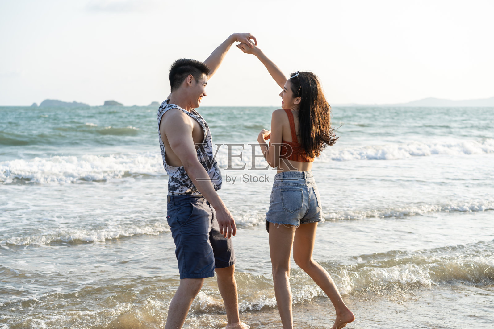 亚洲年轻男女在沙滩上玩得很开心。迷人的新婚夫妇感到快乐，在海边散步和跑步，享受假期，蜜月旅行在热带海岛。照片摄影图片