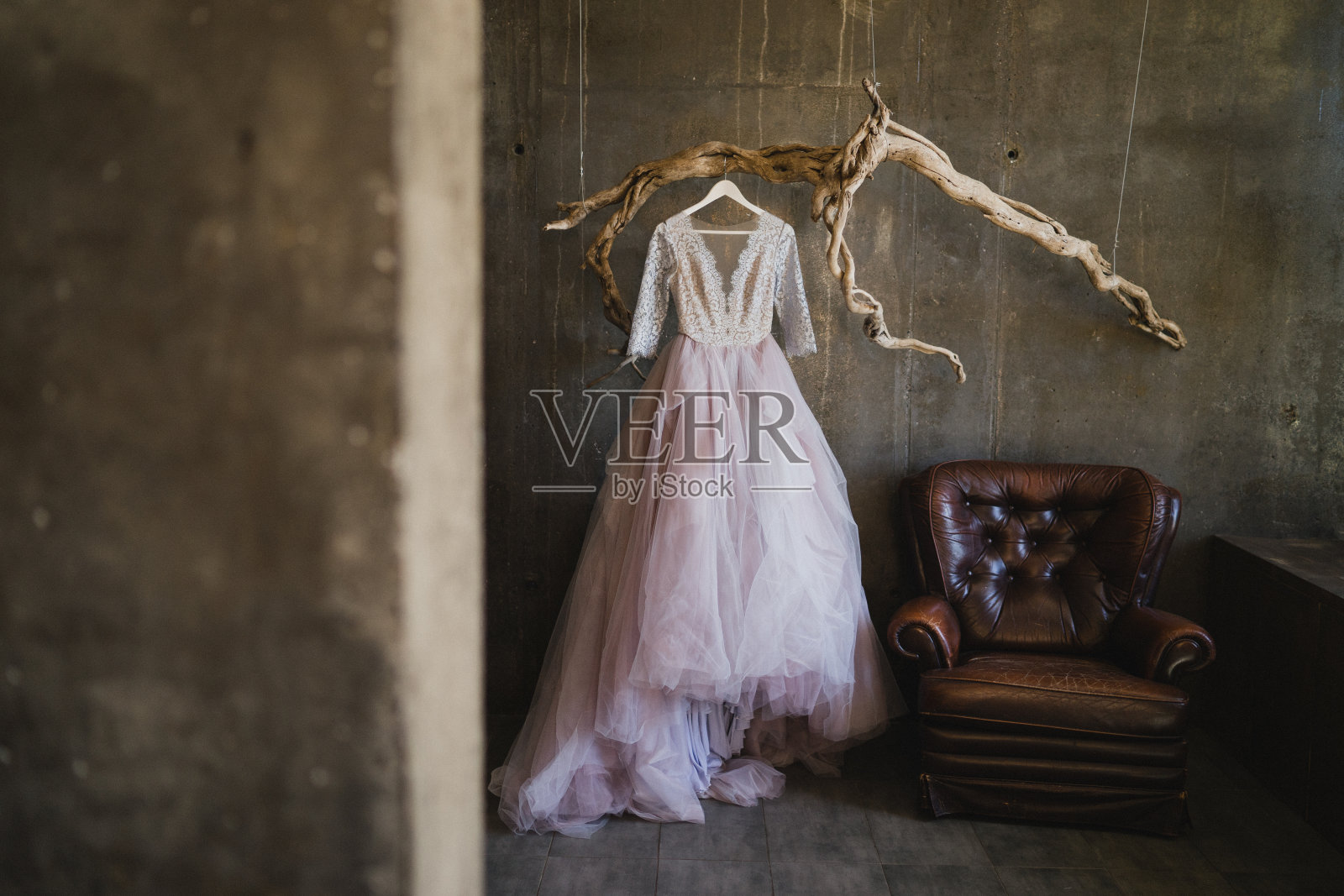 紫色的婚纱挂在混凝土阁楼内部的复古树枝上。照片摄影图片