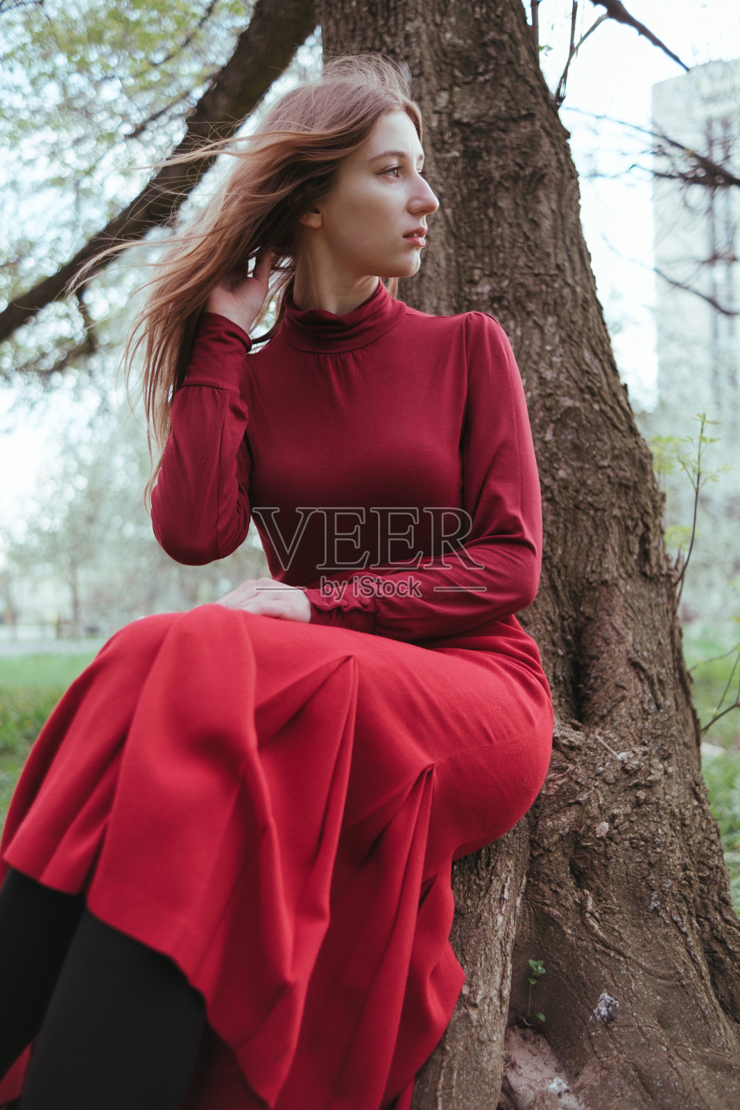 春天的森林里，一个穿红衣服的女孩坐在树下享受大自然照片摄影图片