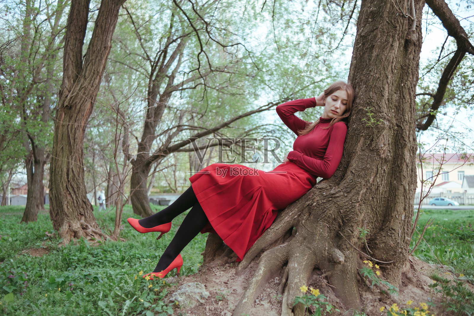 春天的森林里，一个穿红衣服的女孩倚在树上休息照片摄影图片