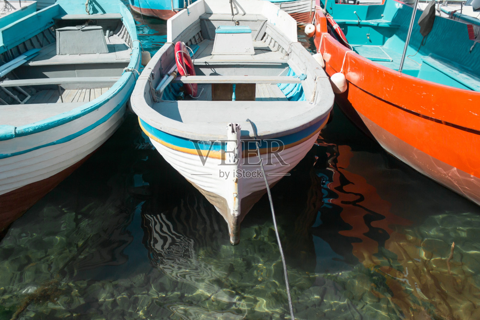 阳光明媚的日子，旧木船停在干净的水面上照片摄影图片