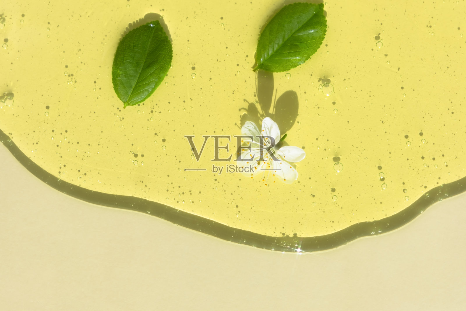 透明的黄色化妆品凝胶或血清，有浅色背景上的白花和绿叶。天然化妆品的概念。前视图。有选择性的重点照片摄影图片