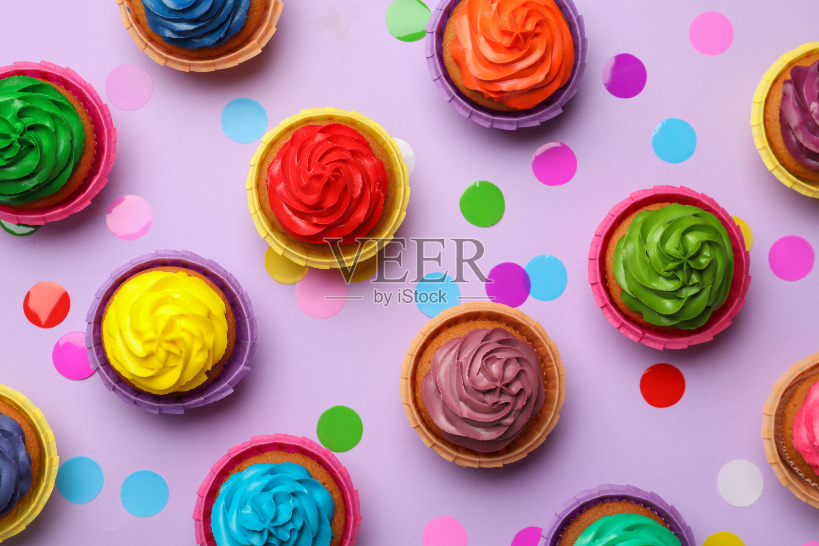 许多美味的五颜六色的纸杯蛋糕和五彩纸屑在紫罗兰色的背景，平铺照片摄影图片