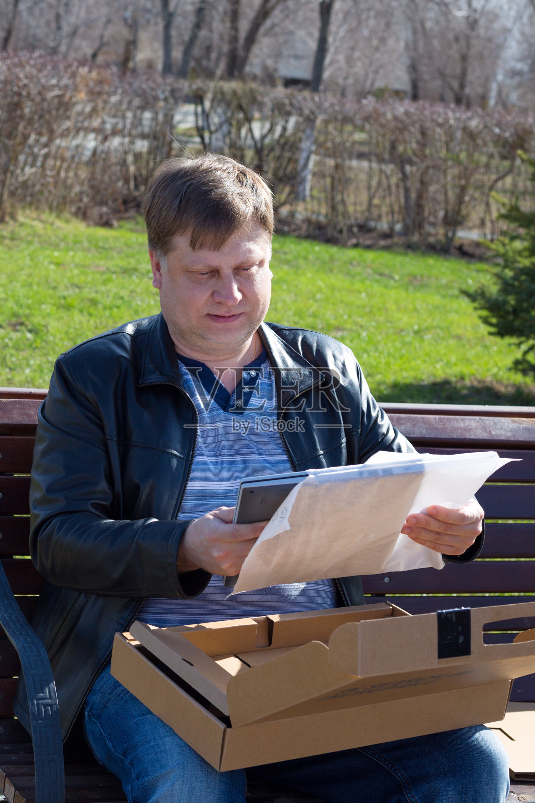 一名40 ~ 44岁的男子坐在长椅上，从盒子里拿出一台新的笔记本电脑照片摄影图片