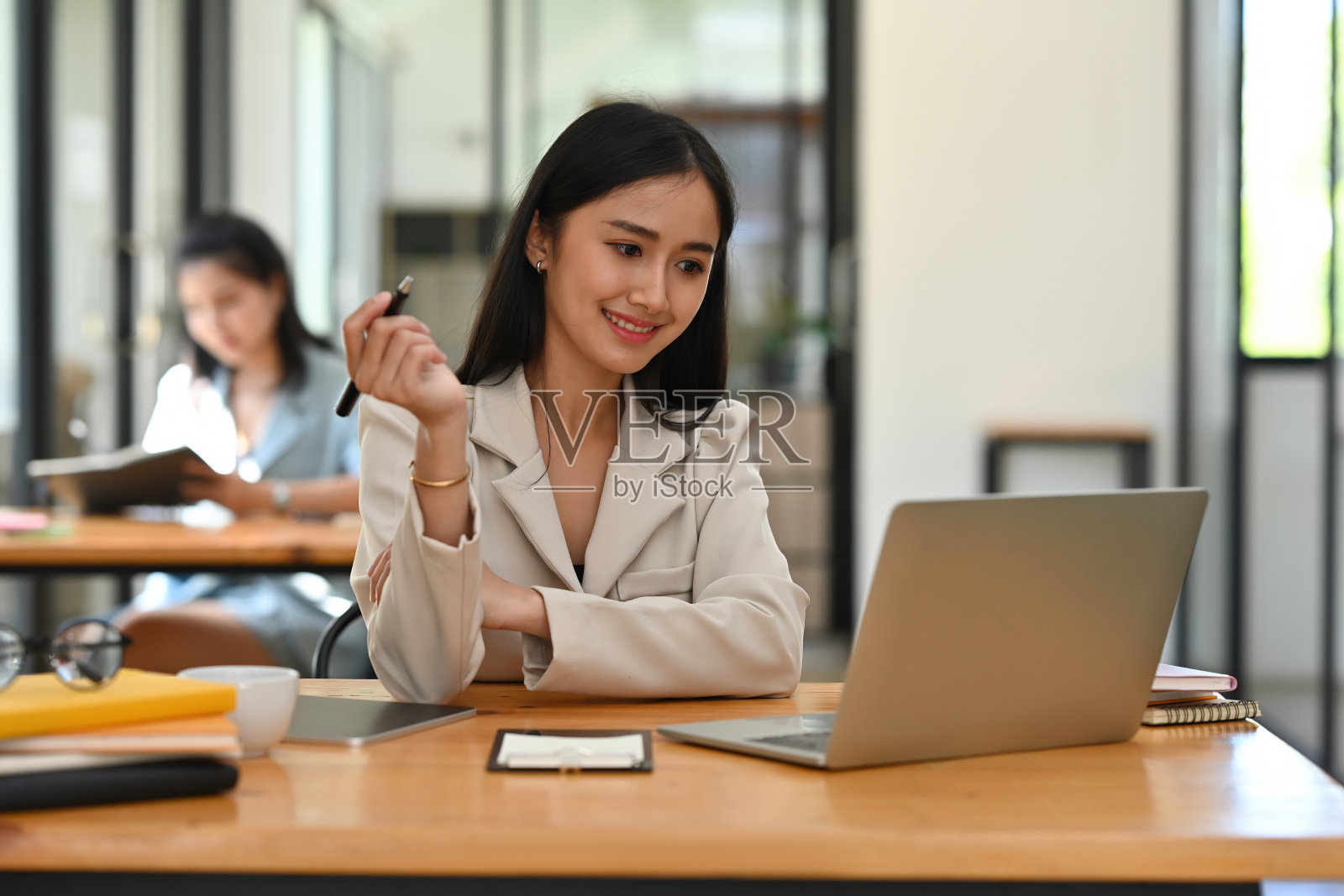 一幅美丽微笑的亚洲女商人的肖像，坐在办公室里，拿着一支笔，在笔记本电脑上工作，为商业和技术概念。照片摄影图片