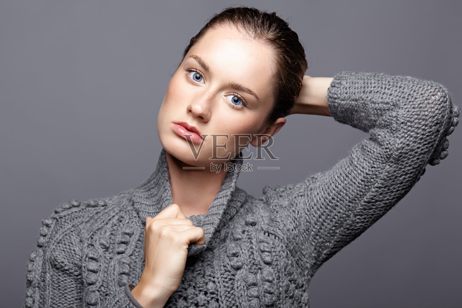 美丽肖像的年轻女子在灰色羊毛毛衣。深色头发的女孩，明亮的蓝色眼睛和日间女性化妆照片摄影图片
