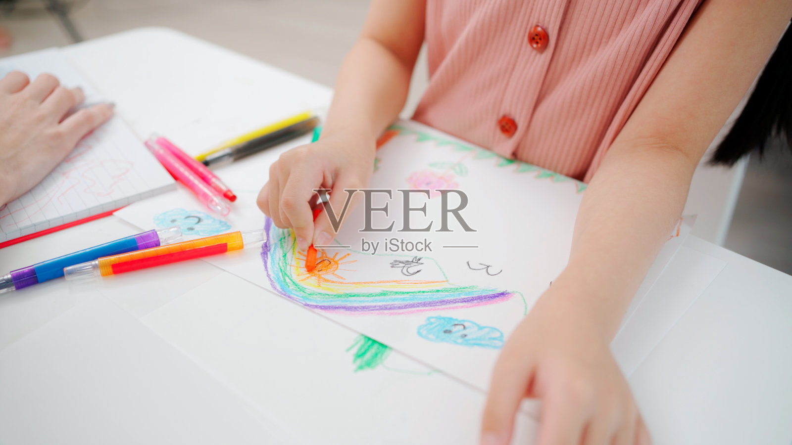 女孩们和老师一起坐在幼儿园的教室里画画。特写孩子画彩虹和油漆颜色。学习、享受、教育、玩的理念。感受快乐和乐趣照片摄影图片