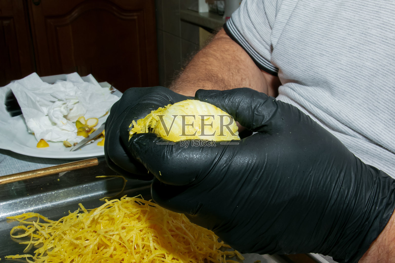 在家里准备柠檬酒的过程。戴着黑色手套的男人用手剥柠檬皮。照片摄影图片