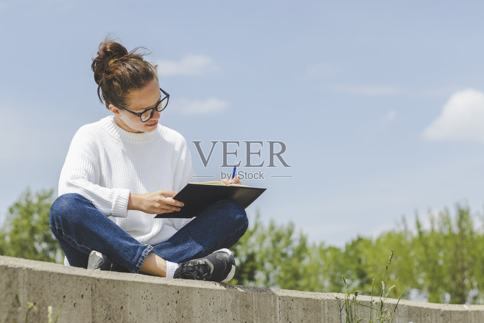 戴眼镜的年轻女子坐在户外，在笔记本上写下了全部内容。照片摄影图片