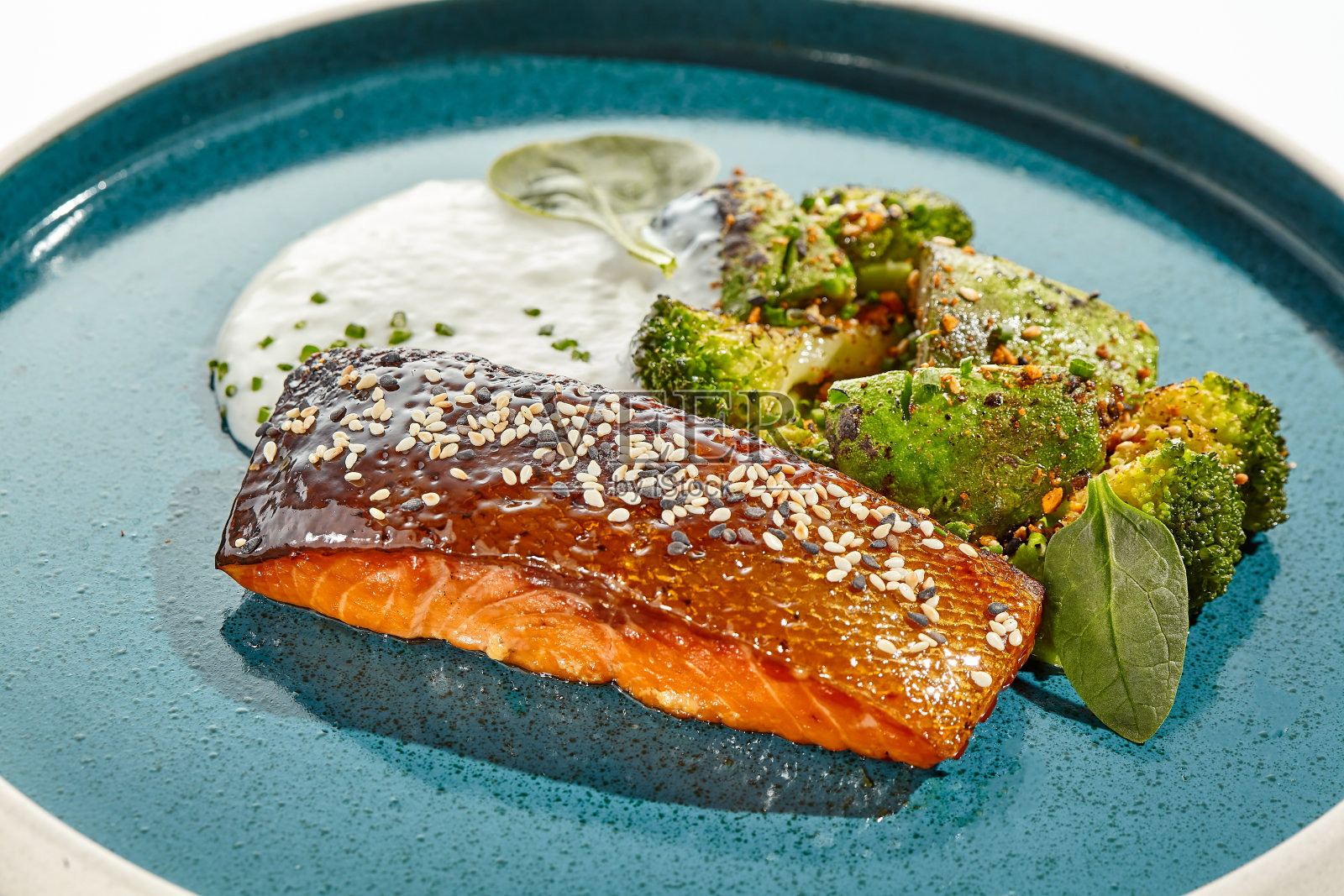 脆皮烤三文鱼，配烤蔬菜和菠菜。烤三文鱼片配花椰菜，牛油果和白酱。生酮食物——带皮的烤鱼和白色底色的绿色蔬菜。照片摄影图片