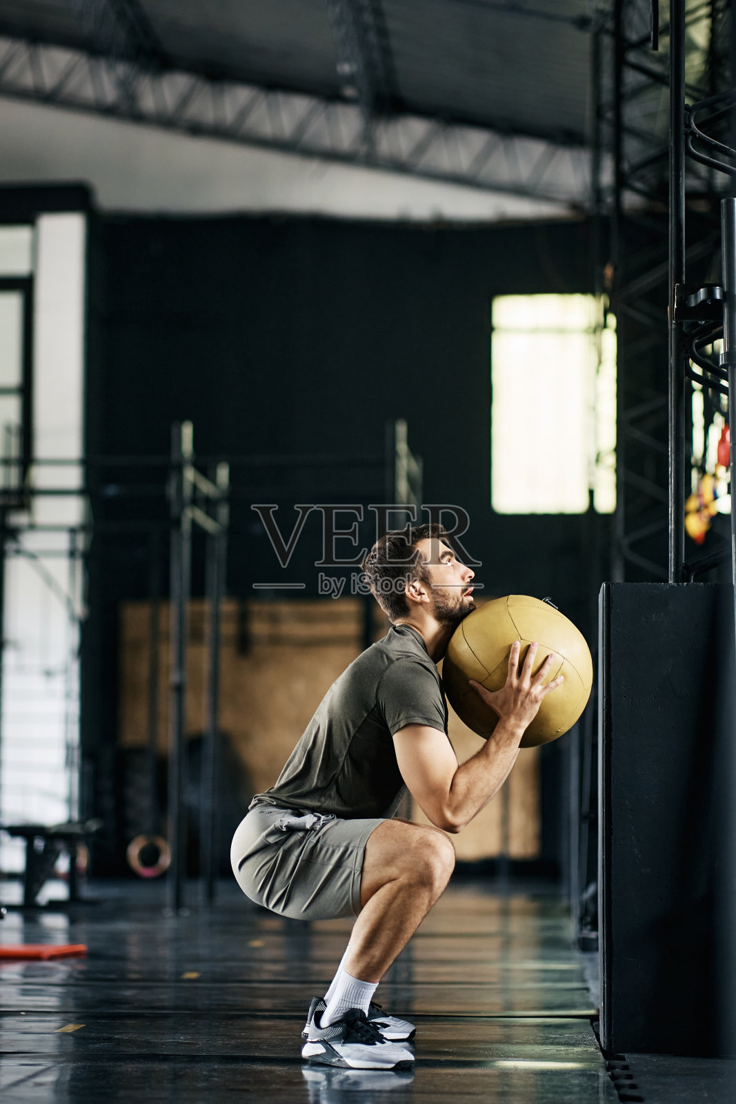 在健身房交叉训练中，运动员拿着健身球做下蹲运动。照片摄影图片
