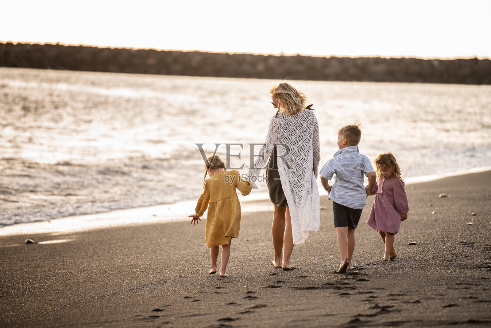 美丽的一家人在沙滩上散步。妈妈和孩子一起度假。完整的长度。照片摄影图片