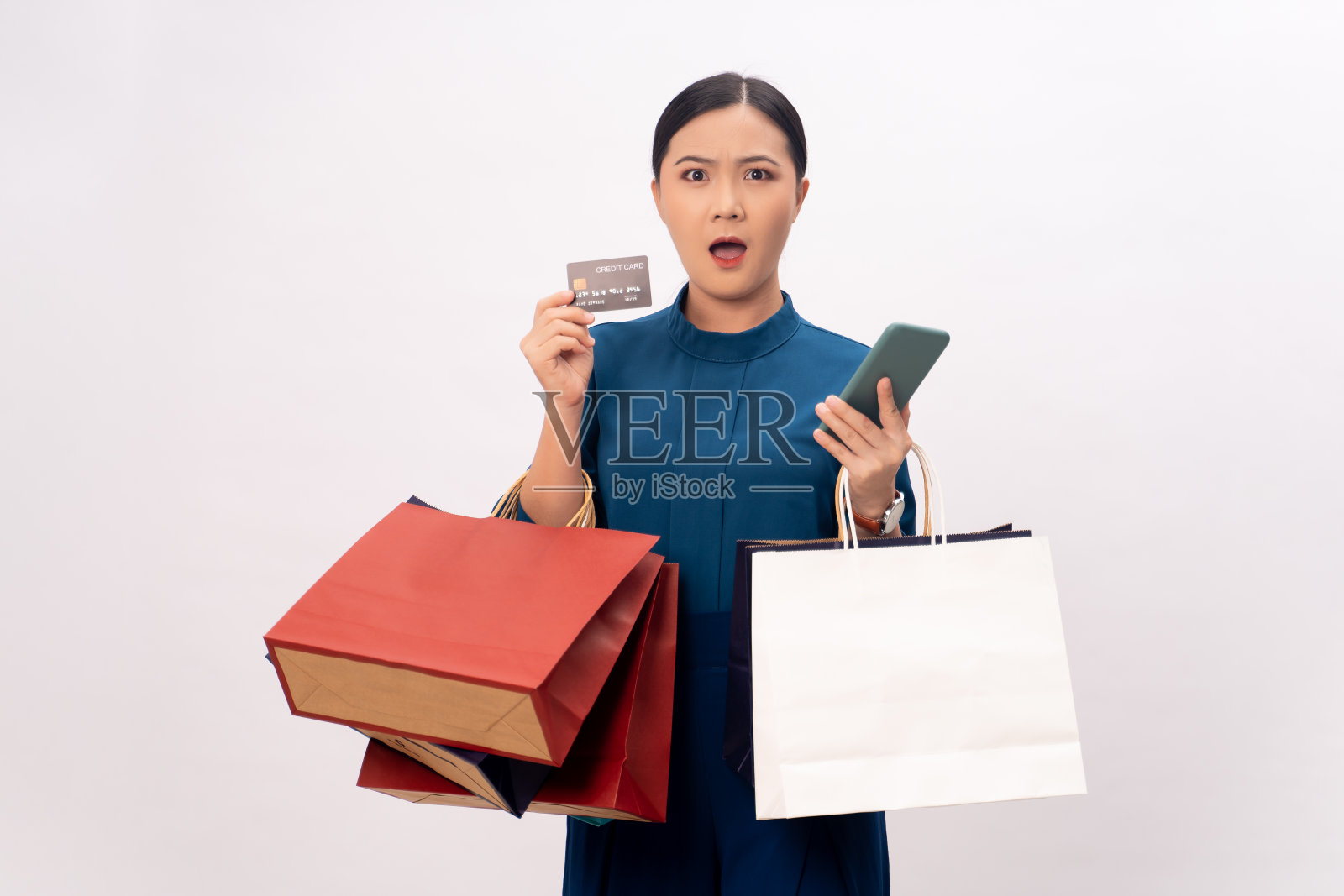 亚洲女性内疚的担心拿着智能手机，信用卡和购物袋模拟隔离在白人背景。照片摄影图片