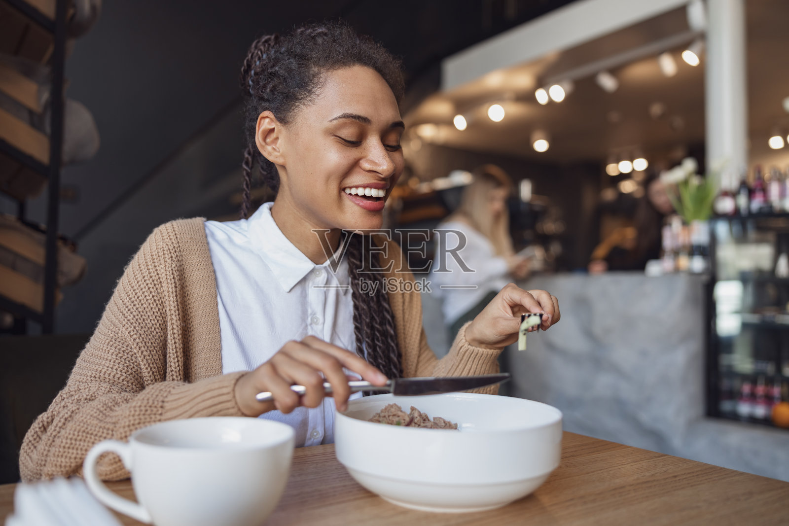 微笑时尚的非洲裔美国年轻女性在时髦的餐厅吃午餐，食物在白色陶瓷餐具照片摄影图片