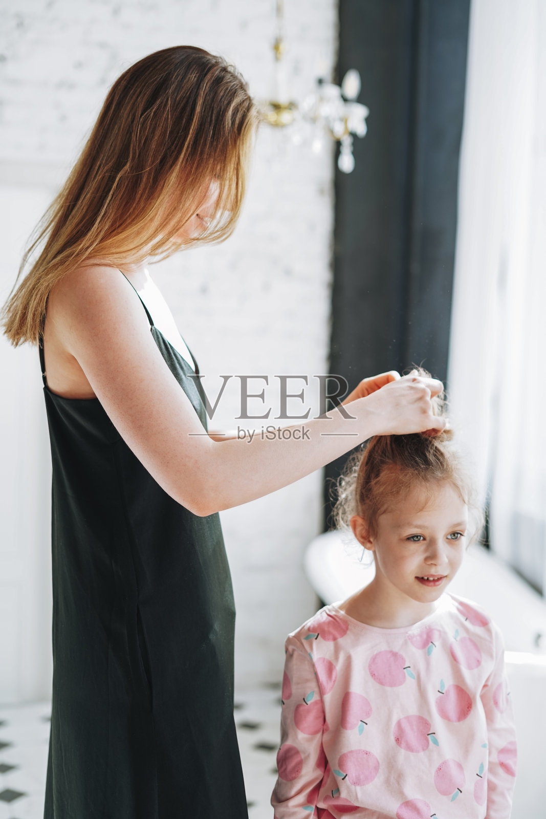 年轻的母亲，长头发的女人在黑色的裙子和小女孩十几岁的女儿在家里玩在早上，家人一起在浴室里度过的时间照片摄影图片