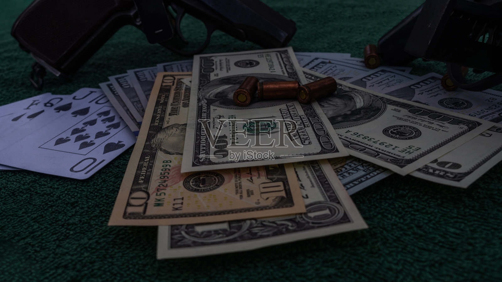 用真钱玩扑克或21点。绿色的桌子上有手枪、弹药、美元和一副扑克牌。照片摄影图片