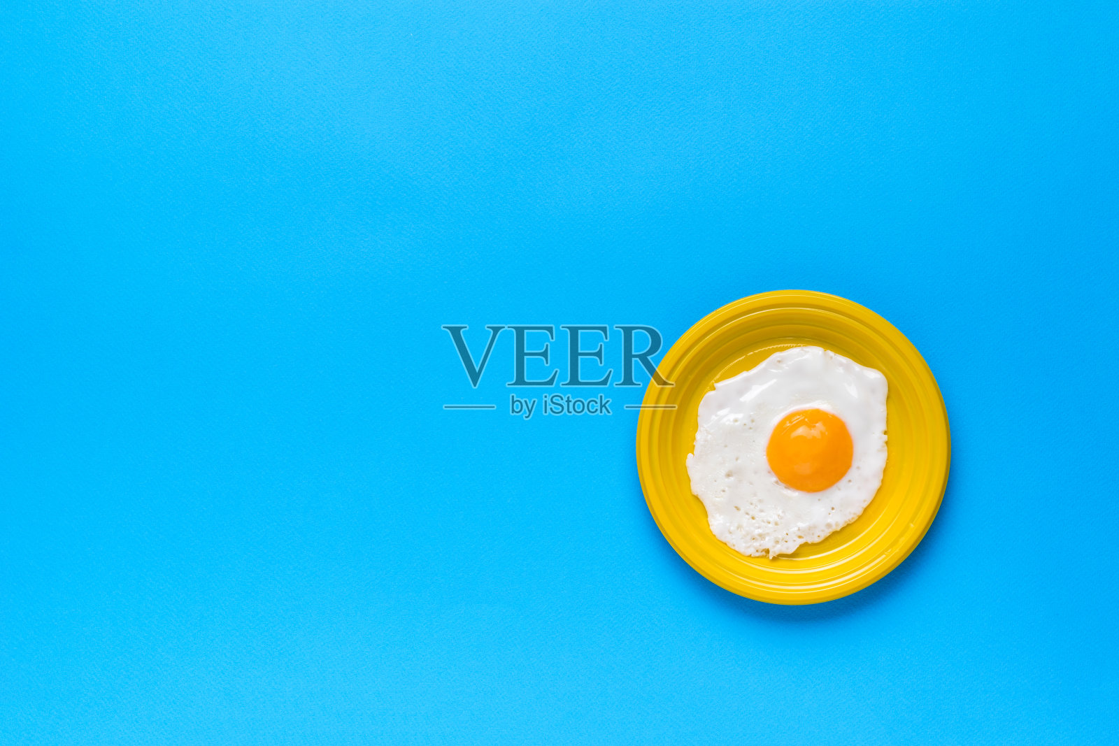 蓝色底色，黄色碗里的新鲜煎蛋。一个受欢迎的早餐。最小的概念。一个受欢迎的早餐。照片摄影图片